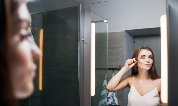 Frau beim Augenbrauenputzen vor einem Badezimmerspiegel — Stockfoto