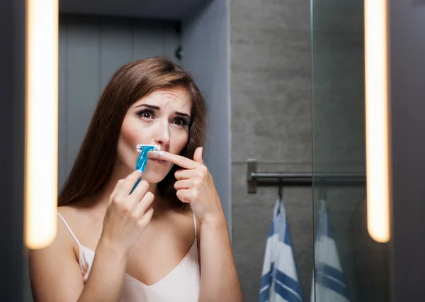 Woman shaving mustache in front of a bathroom mirror — Stock Photo, Image