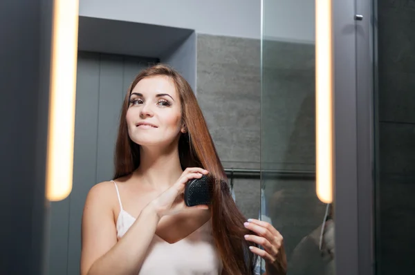 Mujer cepillarse el cabello delante de un espejo de baño —  Fotos de Stock