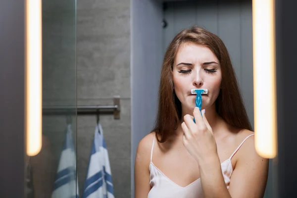 Woman shaving mustache in front of a bathroom mirror — Stock Photo, Image