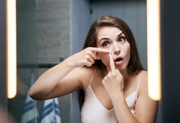 Женщина сжимает прыщи перед зеркалом в ванной — стоковое фото