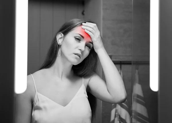 Woman with headache in front of a bathroom mirror — Stock Photo, Image