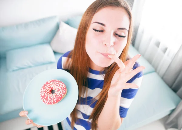 Mulher em casa comendo donut e lambendo o dedo — Fotografia de Stock