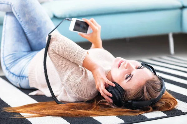 Женщина в наушниках лежит и слушает музыку дома — стоковое фото