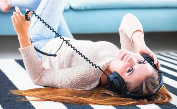 Mulher com fones de ouvido mentindo e ouvindo música em casa — Fotografia de Stock