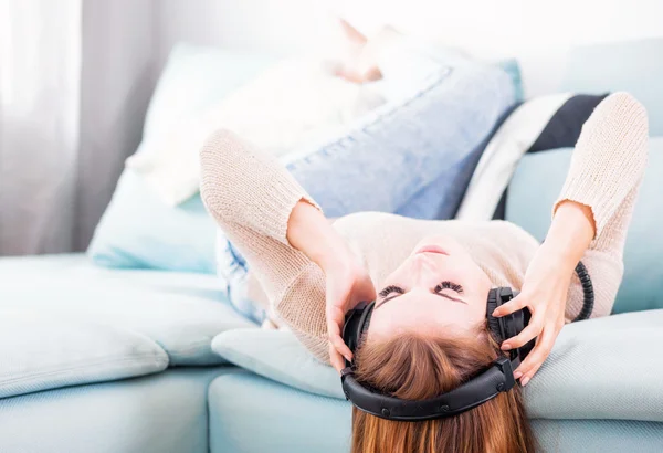 Vrouw met hoofdtelefoon liegen en luisteren naar muziek thuis — Stockfoto