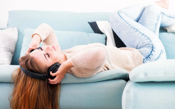 Mulher com fones de ouvido mentindo e ouvindo música em casa — Fotografia de Stock