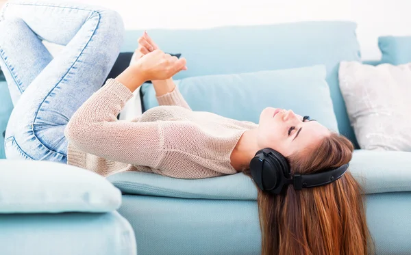 Mulher com fones de ouvido mentindo e ouvindo música em casa — Fotografia de Stock