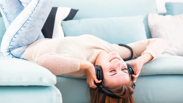 Vrouw met hoofdtelefoon liegen en luisteren naar muziek thuis — Stockfoto