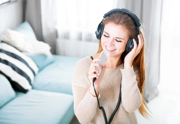 Vrouw met hoofdtelefoon zingen en luisteren naar muziek thuis — Stockfoto