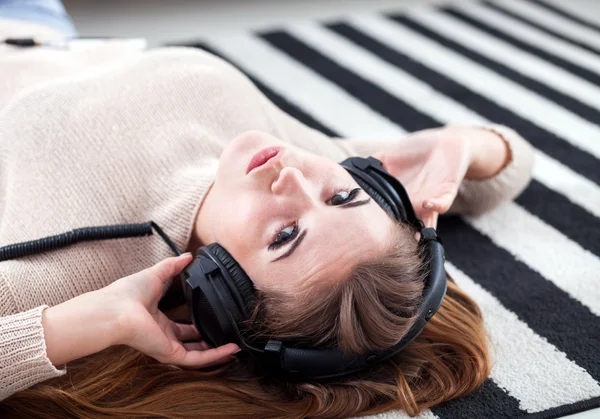 Vrouw met hoofdtelefoon liegen en luisteren naar muziek thuis — Stockfoto