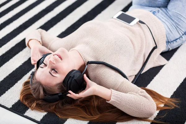 Vrouw met hoofdtelefoon liegen en luisteren naar muziek thuis — Stockfoto