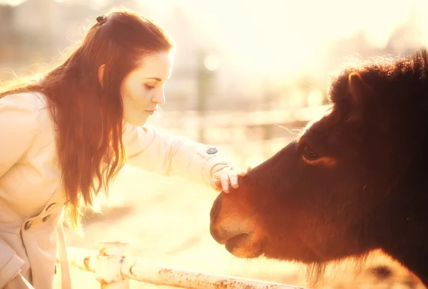 Young woman stroking pony in mini zoo — Stock Photo, Image