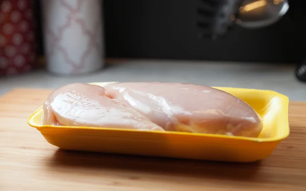 Råa kycklingbröst filéer i paket på träskiva — Stockfoto
