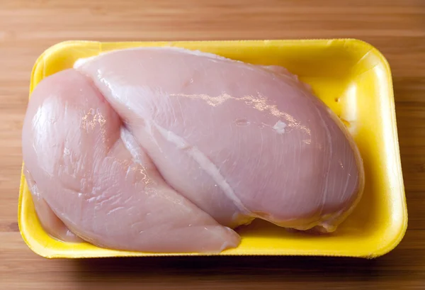 Råa kycklingbröst filéer i paket på träskiva — Stockfoto
