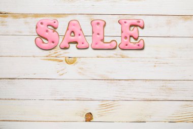 Beyaz ahşap masa üstünde pembe ev yapımı zencefilli bisküvilerden yapılan satış sözcüğü. Boşluğu kopyala.