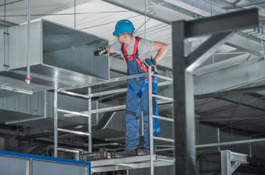 HVAC Profesyonel Teknisyen Yeni İnşa Edilen Metal Hava Kanalı Ticari Depo Binasına Bakıyor.