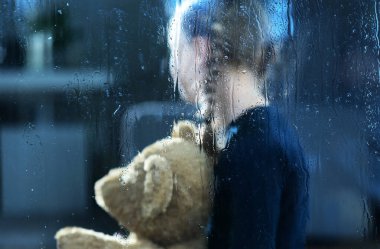 Pencerenin Arkasında Ayı Teddy 'nin oynadığı kız Yağmur Damlaları tarafından korunuyor. Çocuk Depresyonu ve Sosyal Sorunlar Kavramsal Fotoğraf.