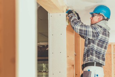 İnşaat endüstrisi teması. 40 'larında Kafkasyalı Profesyonel Elektrikçi tarafından Tahta Ev Yapısı İçinde Elektrik Hattı Kurulumu.