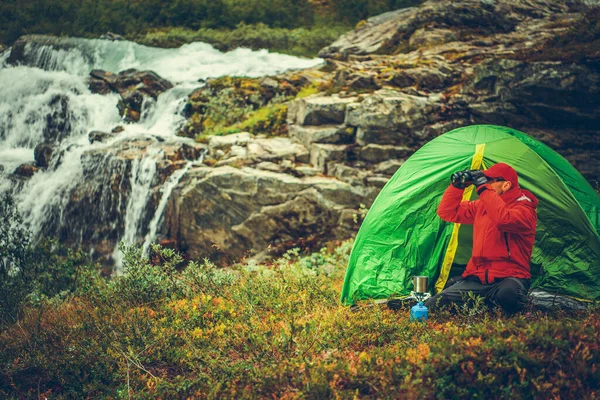 白种人在帐篷前用双筒望远镜发现东西 以瀑布为背景的风景景观 野性营地 — 图库照片