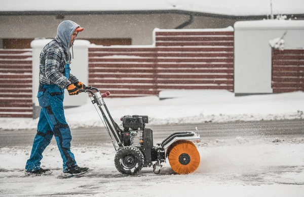 Caucasian Men Cleaning Driveway and Removing Fresh Fallen Snow Using Powerful Gasoline Brush Broom.