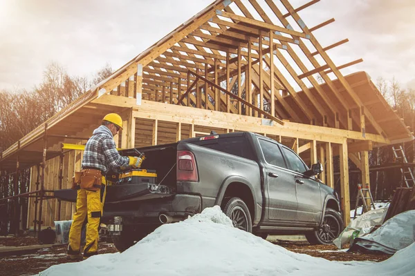 Contractor Worker in Yellow Hard Hat Preparing For His Shift Next to His Pickup Truck. Residential House Wood Structure Construction Zone.