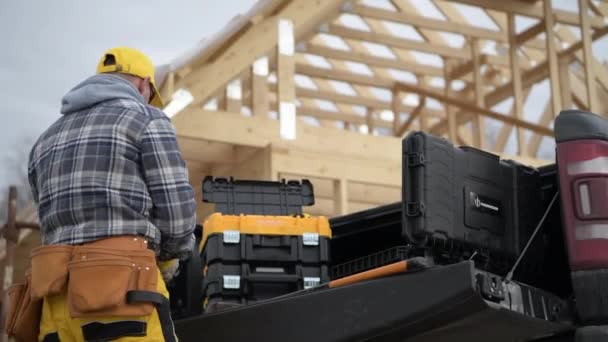 彼の40代の白人建設業者と彼の近代的なブラックピックアップトラック 男性は仕事のためにツールを準備します 木の家の骨格の背景 — ストック動画