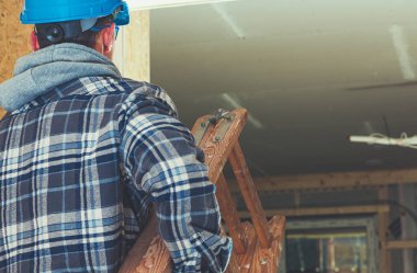 Ellerinde tahta merdiven olan inşaat işçisi yeni inşa edilen evin içindeki başka bir odaya malzeme taşıyor..