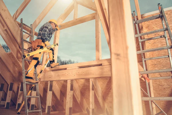 Second Level of Wooden Skeleton Frame of House Construction. Professional Industry Worker with Spirit Level Tool in His Hand. Industrial Theme.