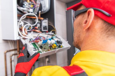 Modern Merkezi Gaz Isıtıcı Elektronik Tamiri. Kafkasyalı HVAC teknisyeni ısıtıcının içine bakıyor. Endüstriyel Tema.