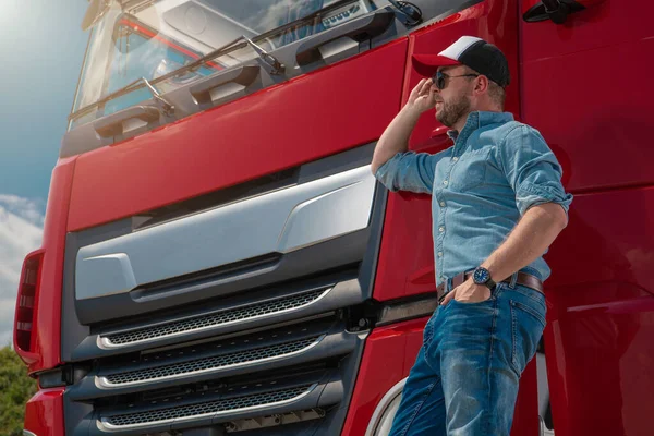 Caucasian Euro Semi Truck Driver in Front of His Brand New Red Truck Tractor. Automotive and Heavy Duty Transportation Industry Theme.