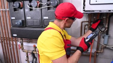 Ellerinde doğal gaz dedektörü olan profesyonel gaz ısıtma teknisyeni ısıtma fırınının içinde potansiyel sızıntı arıyor..