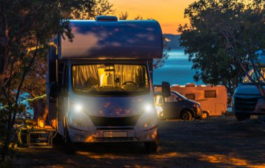Manzaralı karavan kampı günbatımı. Modern Kamp Vans Gece Kalışına Hazırlandı. Arka planda Denizin Üzerindeki Son Işık Çağrısı.