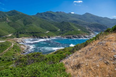 Bright blue ocean waves crash against rocky shores under clear skies. Corsica Island France.