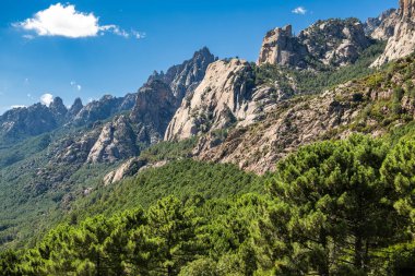 Majestic Corsica Island rocky mountains rise above lush green forests on a sunny day, showcasing nature's beauty