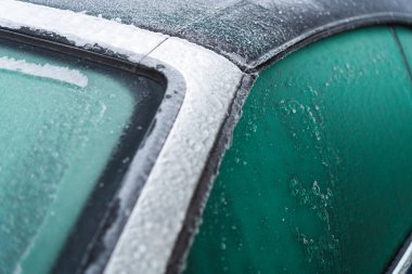 A layer of frost covers the side window of a car parked outside in a chilly urban environment during the early morning hours.