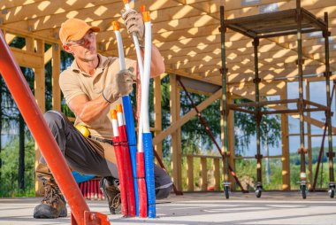 İnşaat işçisi parlak gün ışığında ahşap iskeletin altındaki renkli boruları dikkatlice yerleştirdi..