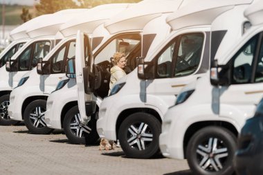 Genç bir kadın karavanın yanında kapısı açık duruyor güneşli bir günde açık hava pazarında aracı inceliyor..