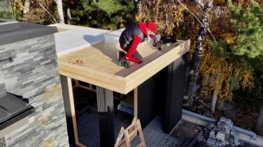 İşçiler parlak bir sonbahar gününde renkli yapraklarla yapıyı hazırlarken çatıya malzeme yerleştiriyorlar.