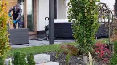 Bir insan arka bahçede bir jakuzinin yanına mobilya taşıyarak dışarıyı temizler..