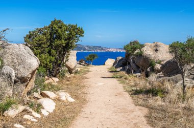 İtalya 'nın Sardunya kentindeki deniz manzarasına götüren, kayalar ve çalıların arasından geçen kirli bir patika.