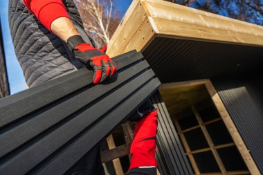 İki işçi güneşli bir günde açık havada bir yapı inşa ederken tahta kaldırıyor..