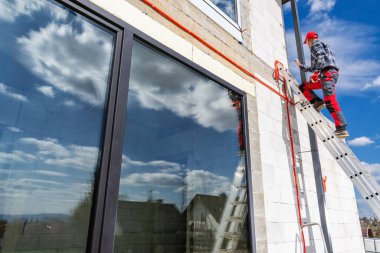Bir işçi boya yapmak için binanın üst kısmına ulaşmak için bir merdiven kullanır. Sahne bulutlu güneşli bir günde meydana gelir..