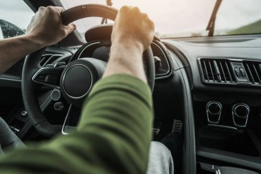 Bir insan ıslak bir yolda sürerken direksiyon simidini tutar..