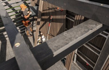 Cihazlar yakınlarda düzenlenirken, inşaat halindeki bir binaya paneller yerleştiren bir işçi bir çerçevenin üzerinde duruyor.