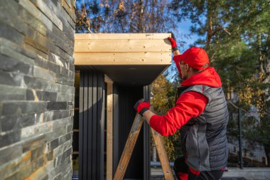 Bir kişi merdivenin üstünde, evin yakınındaki bir binaya odun ekliyor..