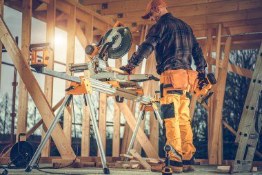 Bir işçi inşaat alanında bir testereyi çalıştırıyor ve gece ışığı binanın çerçevesinden içeri doğru parlıyor..