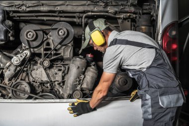 Birisi garajda dizel bir otobüs motoru tamir ediyor. Cihazlar ve ekipmanlar yakında. Ayarlar yoğun ve pratik..