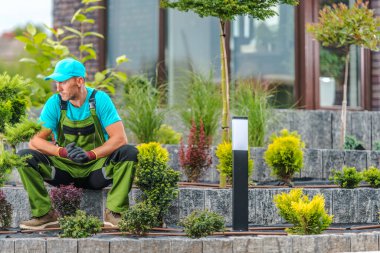 Bir bahçıvan, gündüz vakti çeşitli bitkilerle çevrili taş basamaklarda dinlenir..