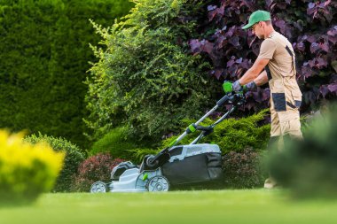 Bir insan açık gökyüzü ile öğleden sonra yeşil bir bahçede çim biçer..